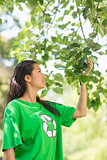 Woman in green recycling t-shirt touching leaves at park