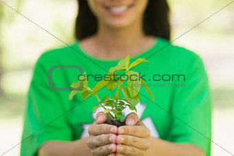 Mid section of woman in recycling t-shirt holding young plant