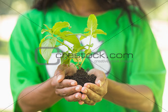 Mid section of woman in green recycling t-shirt holding young plant