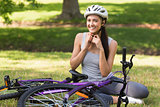 Cheerful woman wearing helmet besides bicycle in park