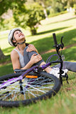 Female bicyclist with hurt leg sitting in park