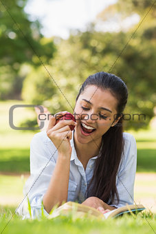 Woman eating apple while reading a book in park