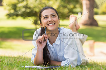 Thoughtful woman with book and pen relaxing in park