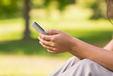 Mid section of woman text messaging in park