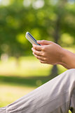 Mid section of a woman text messaging in park