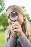 Cute young girl looking through magnifying glass at park