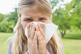Girl blowing nose with tissue paper at park