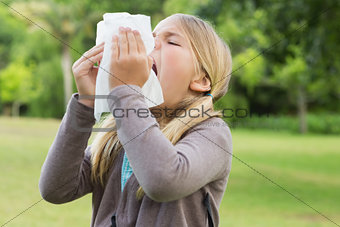 Girl sneezing into tissue paper at park