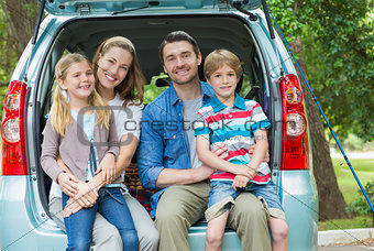 Portrait of happy family of four sitting in car trunk