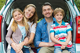 Portrait of happy family of four sitting in car trunk
