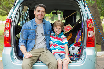 Happy father and son sitting in car trunk