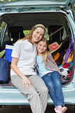 Smiling mother and daughter sitting in car trunk