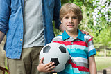 Portrait of a boy holding football besides his father