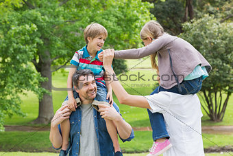 Parents carrying kids on shoulders at park