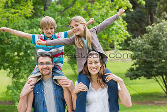 Happy parents carrying kids on shoulders at park