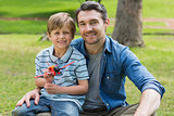 Boy with toy aeroplane sitting on father's lap at park