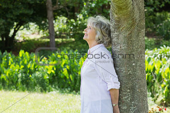Mature woman leaning against tree trunk in park
