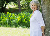 Portrait of mature woman leaning against tree trunk in park