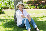 Mature woman sitting against a tree in park