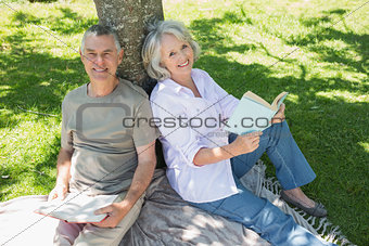 smiling mature couple sitting against tree at park