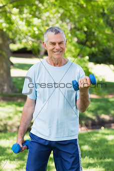 Smiling mature man with dumbbells at park