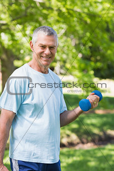 Smiling mature man exercising with dumbbell at park