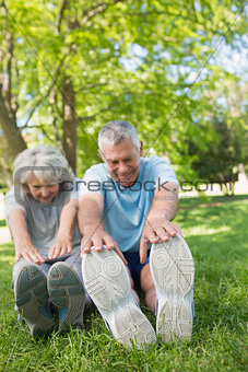Mature couple stretching hands to legs at park