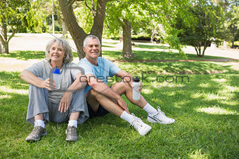 Mature couple sitting with water bottles at park