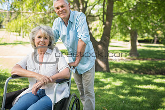 Smiling mature man with woman sitting in wheel chair at park