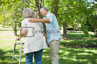 Mature man assisting woman with walker at park