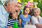 Extended family in party hats blowing birthday cake