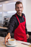Happy young barista putting cup of coffee down on counter