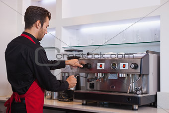 Handsome young barista steaming jug of milk