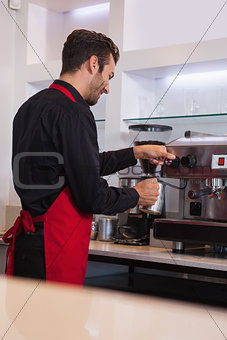 Smiling young barista steaming jug of milk