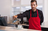Smiling barista pouring milk into cup of coffee