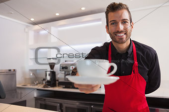 Happy barista offering cup of coffee to camera