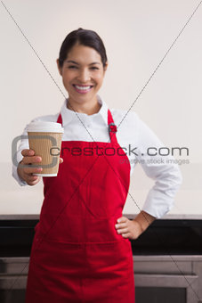 Happy young barista offering cup of coffee to go