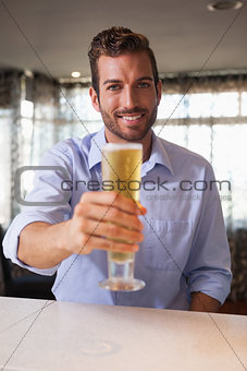 Happy businessman raising glass of beer to camera after work
