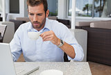 Concentrating businessman working with laptop drinking coffee