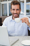 Smiling businessman working with laptop drinking coffee