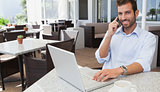 Cheerful businessman talking on phone using his laptop