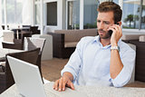 Serious businessman talking on phone using his laptop