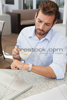 Frowning young businessman checking time holding coffee cup