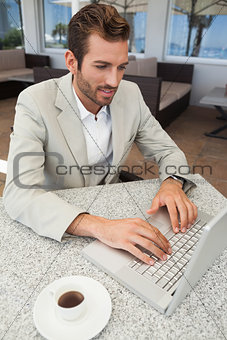 Happy businessman working with his laptop at table having coffee