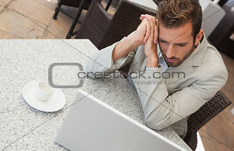 Businessman looking at his laptop at table having coffee