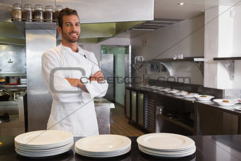 Smiling young chef standing with arms crossed behind counter