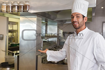 Smiling young chef looking at camera showing his workplace