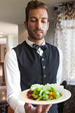 Waiter showing bowl of salad to camera