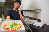 Smiling pizza delivery man taking an order over the phone showing a pizza