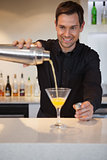 Smiling bartender pouring cocktail into glass